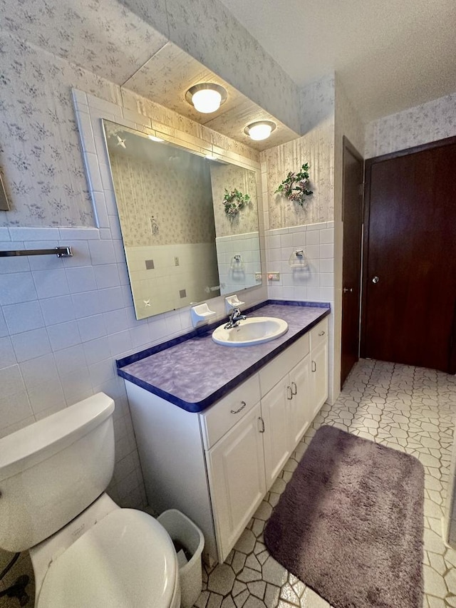 bathroom featuring tile patterned floors, vanity, toilet, and tile walls