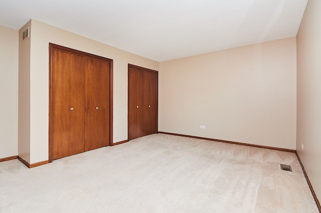 unfurnished bedroom with baseboards, visible vents, two closets, and light carpet