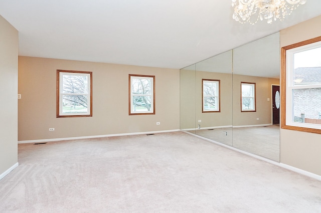 carpeted spare room featuring a notable chandelier, baseboards, and visible vents