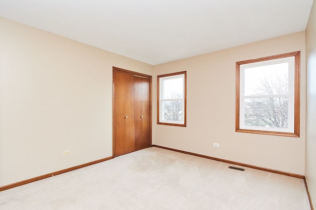 unfurnished room featuring a wealth of natural light, visible vents, light colored carpet, and baseboards