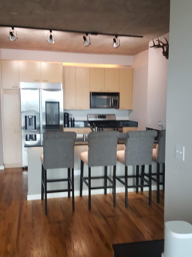 kitchen with a breakfast bar, rail lighting, stainless steel refrigerator with ice dispenser, dark hardwood / wood-style flooring, and range