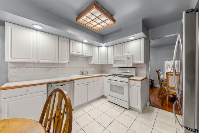 kitchen featuring sink, appliances with stainless steel finishes, tasteful backsplash, light tile patterned flooring, and white cabinetry