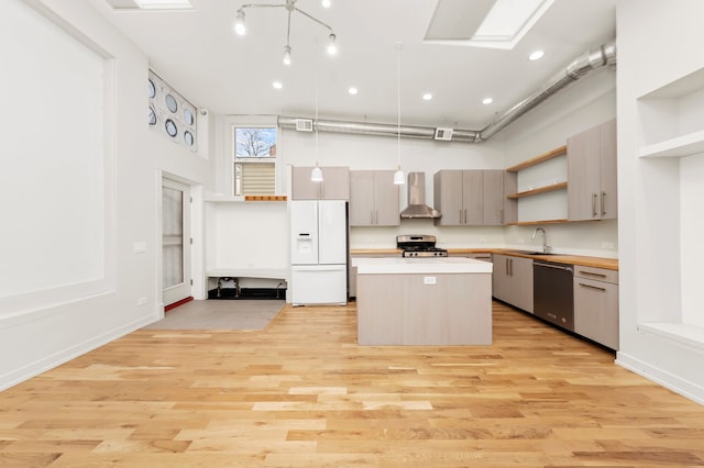 kitchen with wall chimney exhaust hood, stainless steel appliances, sink, light hardwood / wood-style floors, and hanging light fixtures