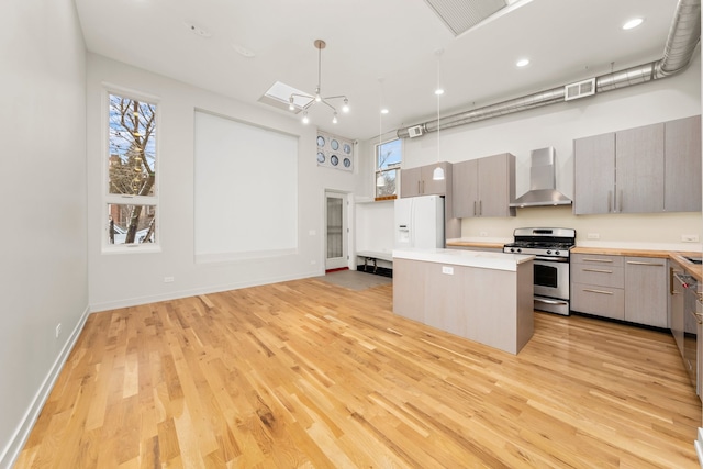 kitchen with pendant lighting, a center island, stainless steel range with gas cooktop, wall chimney range hood, and light hardwood / wood-style flooring