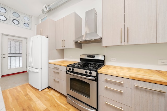 kitchen with wall chimney exhaust hood, gas stove, white refrigerator, light hardwood / wood-style floors, and butcher block counters