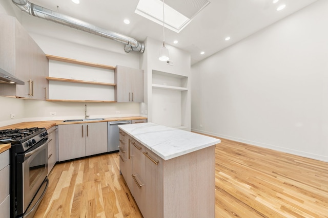 kitchen with a center island, sink, hanging light fixtures, appliances with stainless steel finishes, and light hardwood / wood-style floors