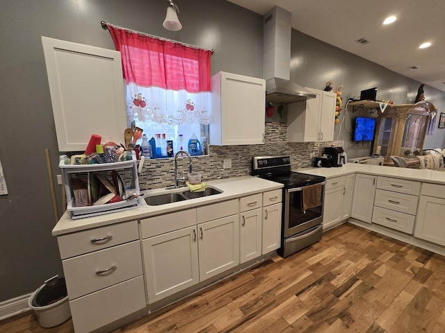 kitchen featuring wall chimney exhaust hood, light countertops, a sink, and stainless steel range with electric stovetop