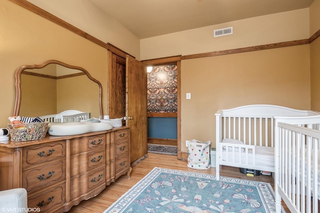 bedroom with light wood-type flooring and a nursery area