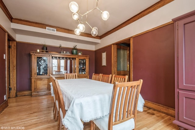 dining area with ornamental molding, a notable chandelier, and light hardwood / wood-style flooring