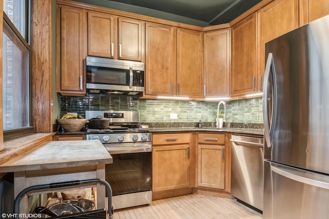 kitchen with stainless steel appliances, sink, dark stone countertops, light hardwood / wood-style floors, and decorative backsplash