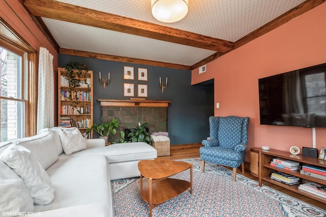 living room featuring a tile fireplace, hardwood / wood-style flooring, and beamed ceiling