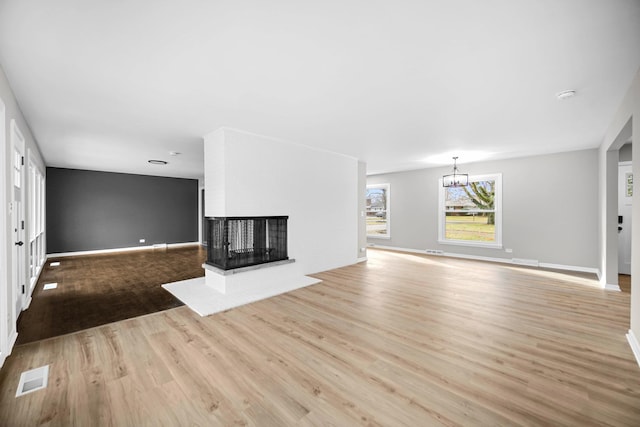 unfurnished living room with a multi sided fireplace, a chandelier, and light hardwood / wood-style floors