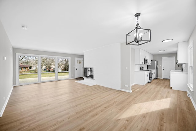 unfurnished living room featuring a multi sided fireplace, sink, light hardwood / wood-style floors, and an inviting chandelier