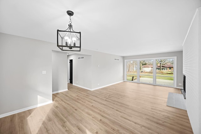 unfurnished living room featuring light wood-type flooring, a fireplace, and an inviting chandelier