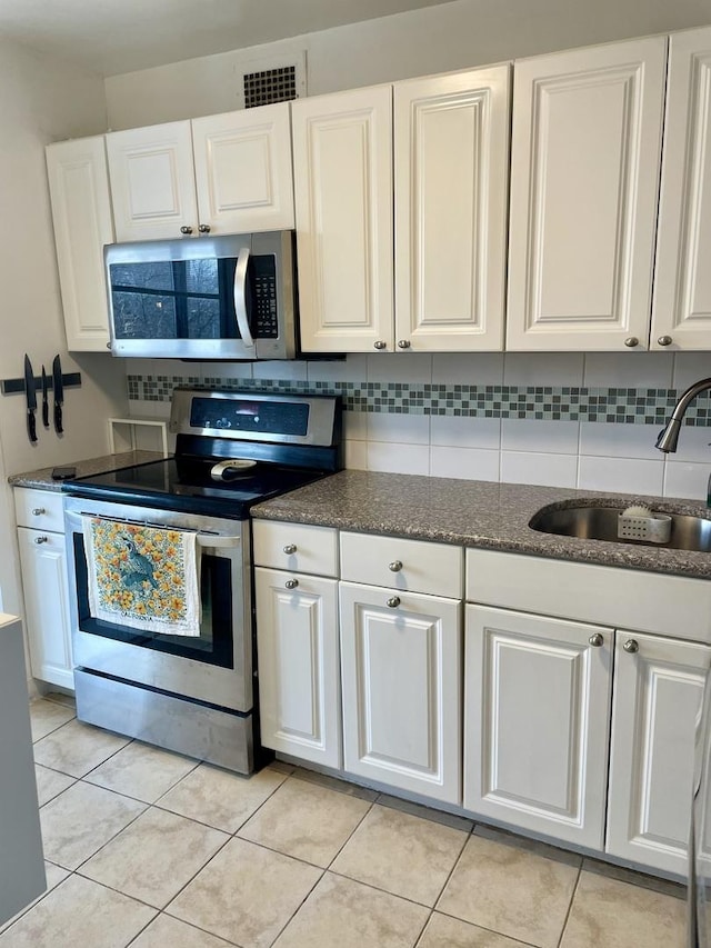 kitchen with sink, stainless steel appliances, light tile patterned floors, backsplash, and white cabinets