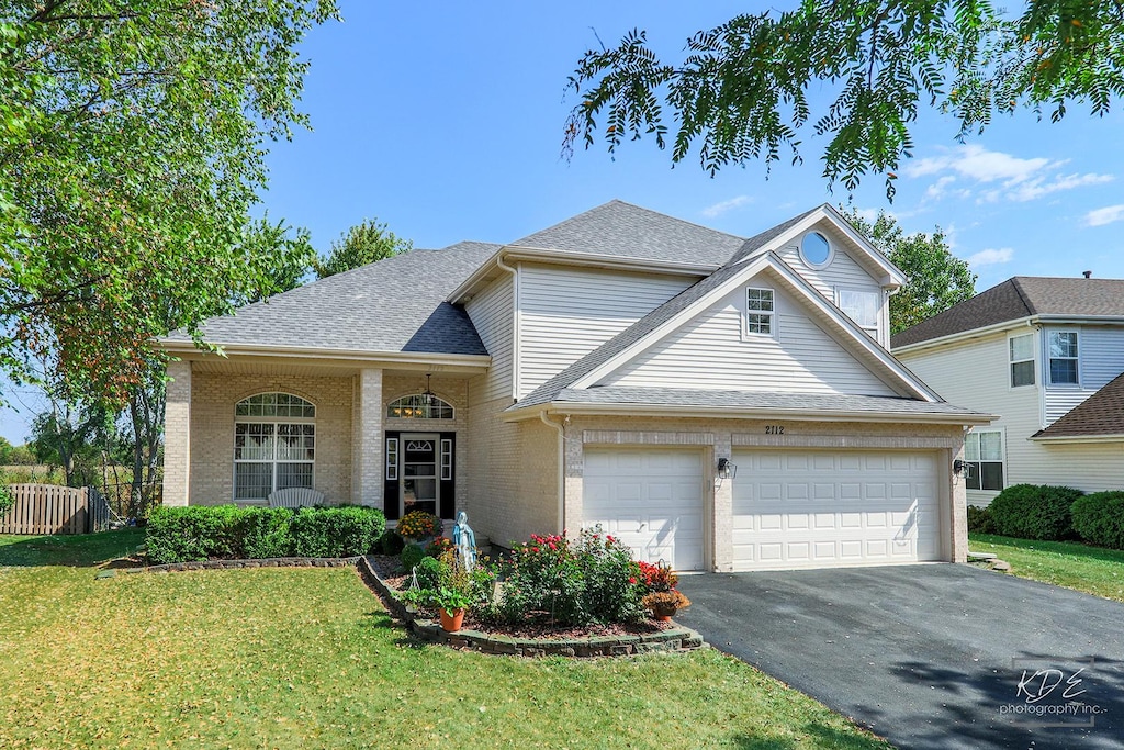 traditional-style house with driveway, brick siding, a shingled roof, fence, and a front yard
