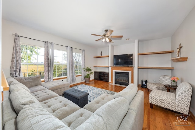 living room featuring a fireplace with flush hearth, a ceiling fan, and wood finished floors