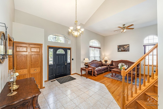 foyer featuring light tile patterned floors, baseboards, stairway, high vaulted ceiling, and ceiling fan with notable chandelier