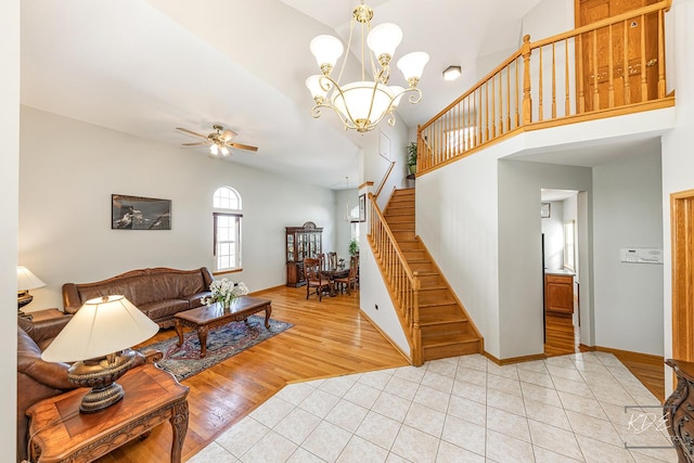 living area with light tile patterned floors, baseboards, stairs, high vaulted ceiling, and ceiling fan with notable chandelier