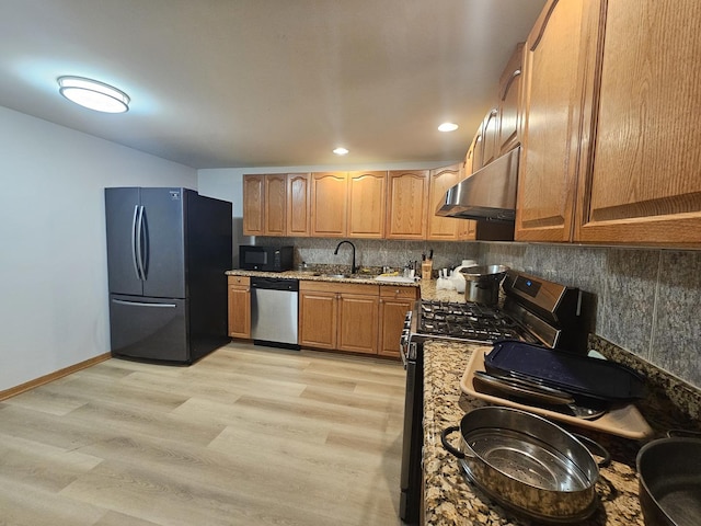 kitchen with tasteful backsplash, appliances with stainless steel finishes, light stone countertops, under cabinet range hood, and a sink