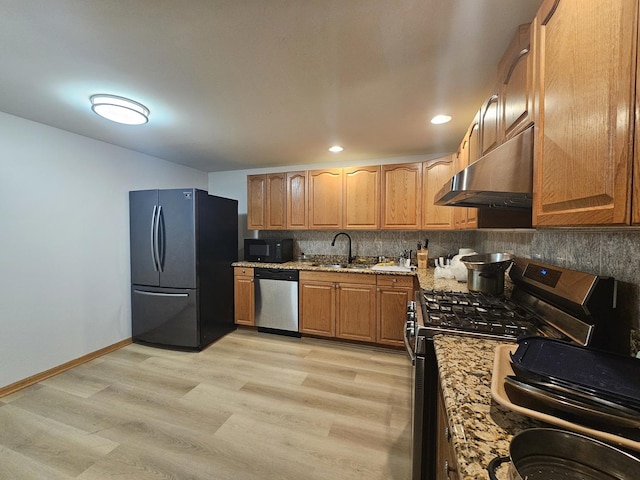 kitchen with under cabinet range hood, a sink, appliances with stainless steel finishes, light stone countertops, and tasteful backsplash