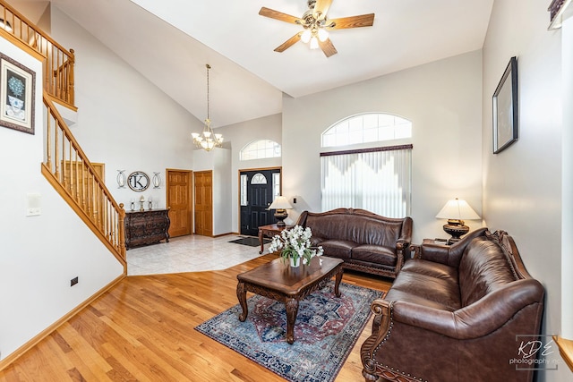 living area featuring baseboards, stairway, light wood-type flooring, high vaulted ceiling, and ceiling fan with notable chandelier