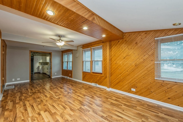 unfurnished living room with hardwood / wood-style flooring, ceiling fan, and wooden walls