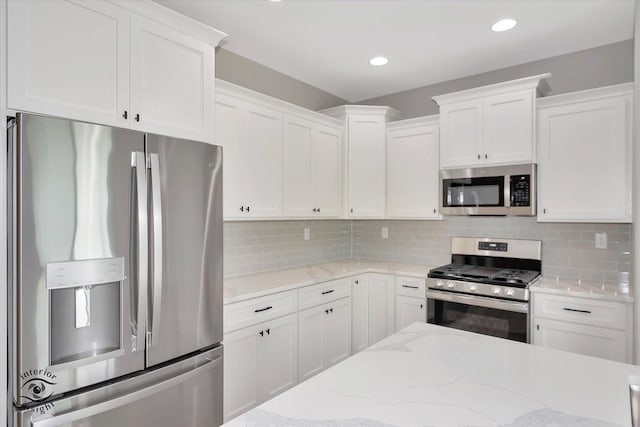 kitchen with decorative backsplash, appliances with stainless steel finishes, white cabinetry, and light stone counters