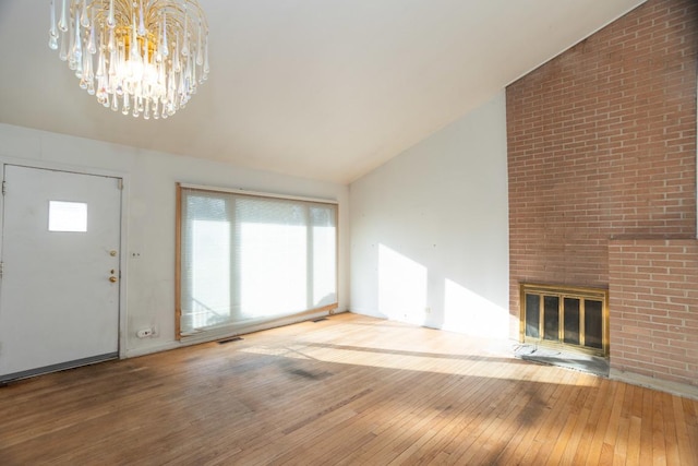 unfurnished living room with hardwood / wood-style flooring, a chandelier, lofted ceiling, and a brick fireplace