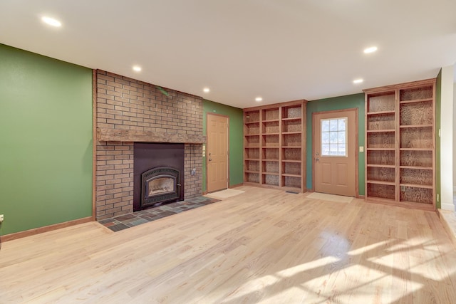 unfurnished living room featuring built in shelves, a brick fireplace, and hardwood / wood-style floors