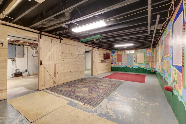 basement with wood walls, a barn door, and electric panel