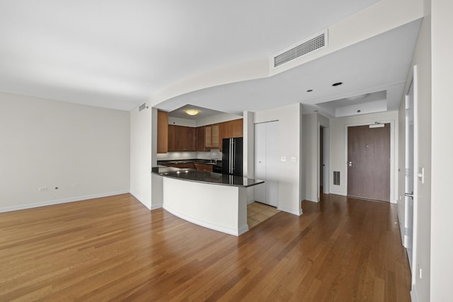 kitchen with black refrigerator, kitchen peninsula, and light wood-type flooring