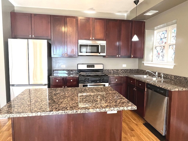 kitchen with sink, appliances with stainless steel finishes, hanging light fixtures, a kitchen island, and dark stone counters