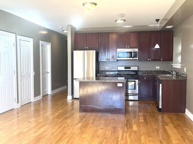 kitchen featuring sink, dark stone countertops, hanging light fixtures, stainless steel appliances, and light wood-type flooring