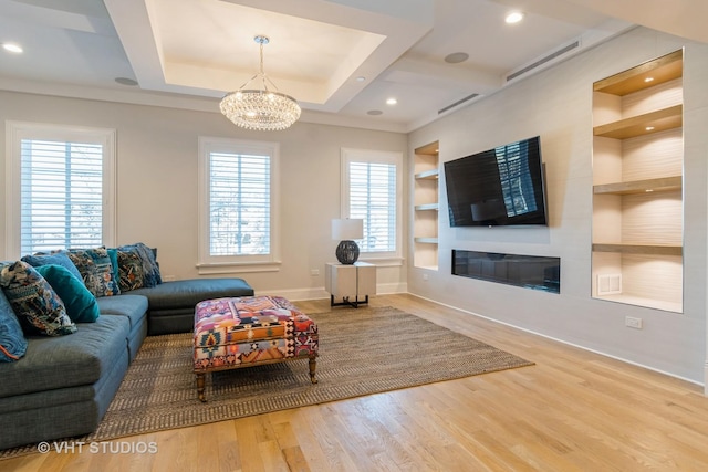 living room featuring a large fireplace, a notable chandelier, plenty of natural light, and built in shelves