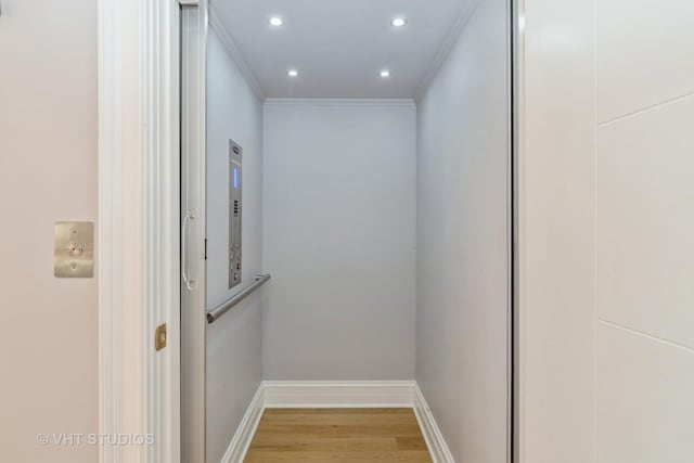 corridor with ornamental molding, elevator, and light wood-type flooring