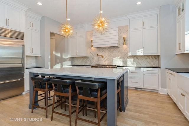 kitchen with built in fridge, white cabinets, a breakfast bar area, hanging light fixtures, and a notable chandelier