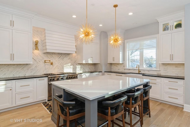 kitchen with stainless steel range, sink, white cabinetry, and hanging light fixtures