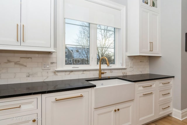 kitchen with sink, white cabinets, light wood-type flooring, decorative backsplash, and dark stone counters