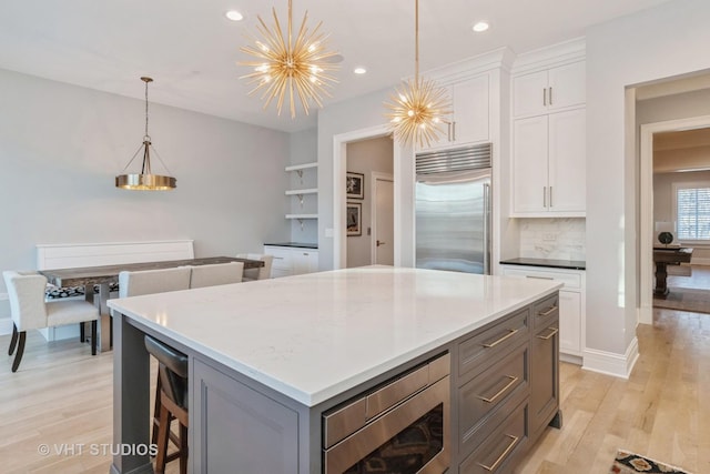 kitchen featuring built in appliances, a center island, hanging light fixtures, decorative backsplash, and white cabinetry