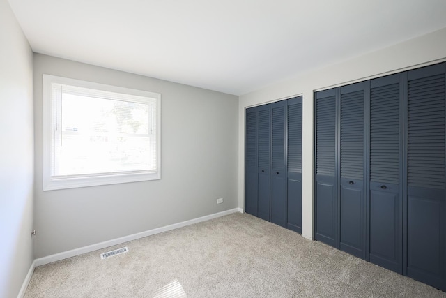 unfurnished bedroom featuring multiple closets and light carpet