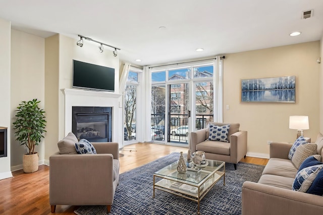 living area featuring wood finished floors, a glass covered fireplace, visible vents, and baseboards