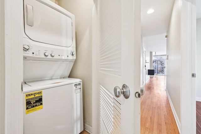 laundry area with stacked washer and dryer, light wood-type flooring, laundry area, and baseboards