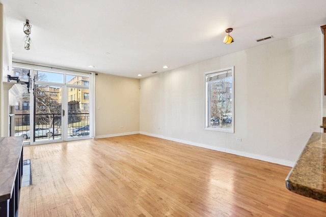 unfurnished living room with light wood-type flooring, plenty of natural light, visible vents, and baseboards