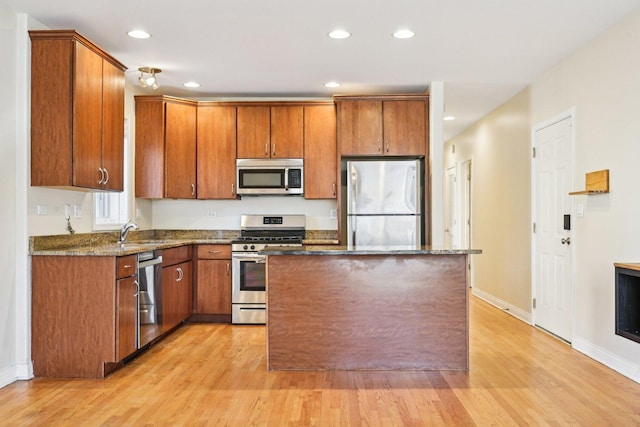 kitchen featuring appliances with stainless steel finishes, a center island, light wood-type flooring, and a sink