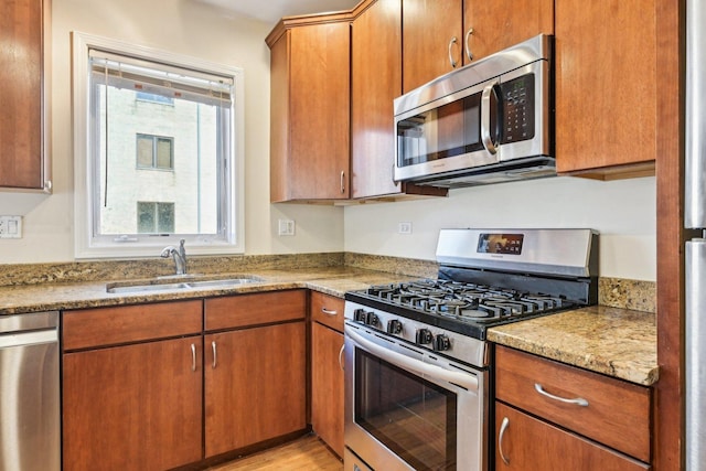 kitchen featuring stainless steel appliances, brown cabinets, a sink, and light stone countertops