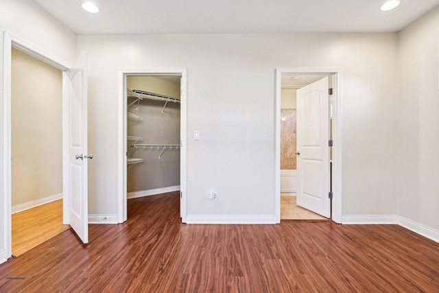 unfurnished bedroom with a spacious closet, a closet, wood finished floors, and baseboards