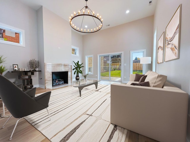 living area with recessed lighting, a notable chandelier, a high ceiling, a high end fireplace, and light wood finished floors