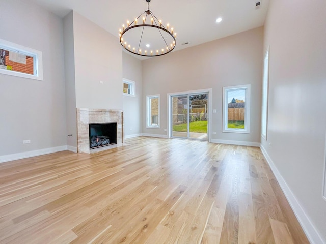 unfurnished living room with light wood finished floors, a premium fireplace, baseboards, and a notable chandelier