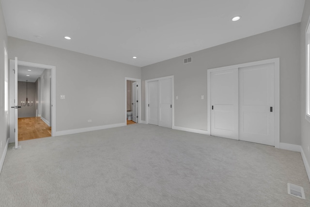 unfurnished bedroom featuring multiple closets, recessed lighting, light colored carpet, and baseboards